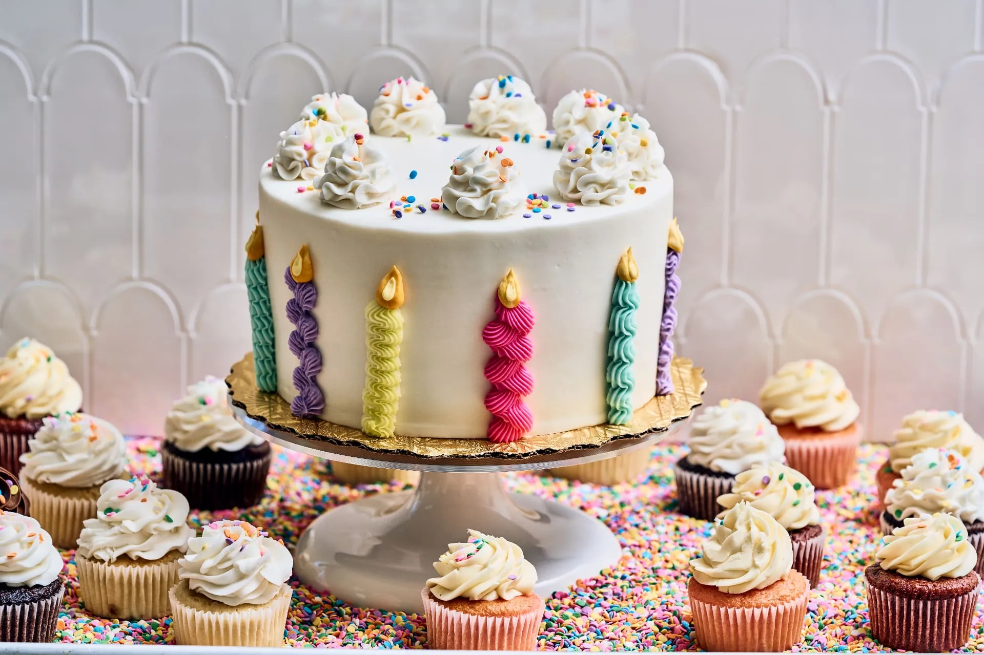 Festive birthday cake with colorful candles and cupcakes