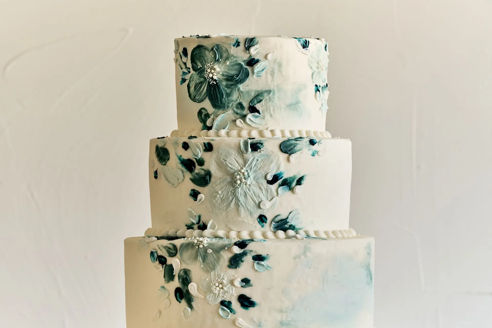 Three-tier wedding cake with elegant teal and white floral decorations