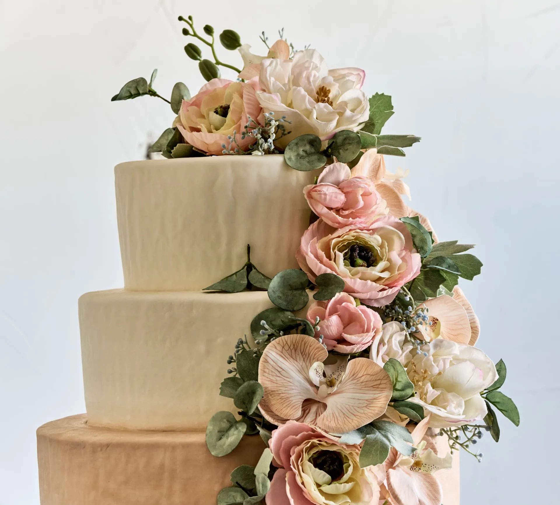 Three-tier wedding cake with beautiful fresh flowers including roses and eucalyptus